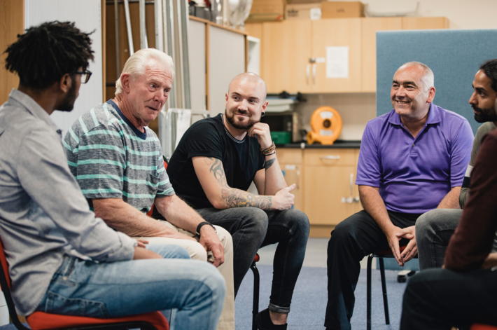 A group of diverse men sit in a circle listening to an older gentleman's story.